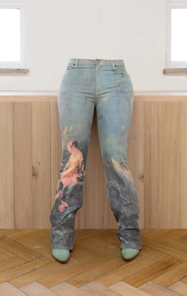 Front of Fiona Abicare's cast pair of legs in blue jeans with a colourful printed image and teal colour boots. The legs are leaning against a ledge in the gallery, self supported by the bottom and thighs of the sculpture.