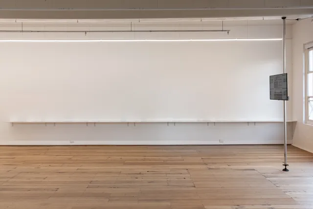 Installation view of 13 Years showing a shelf suspended on the back wall with a series of images placed on it. To the right is a screen suspended at eye level away from the gallery wall. The screen is not legible.