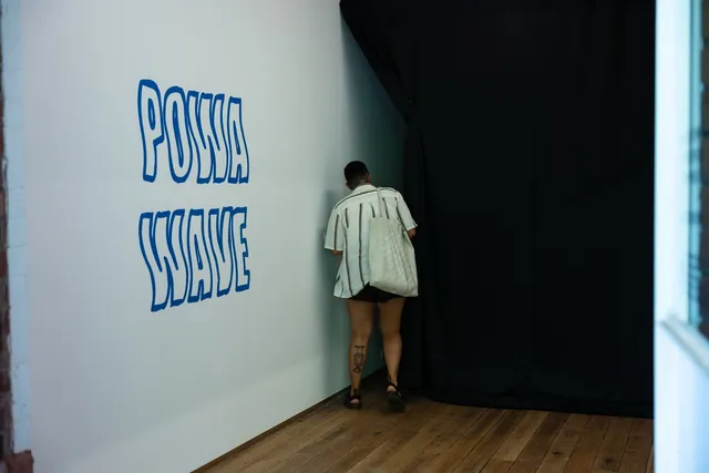 A figure peeking around a black curtain with "POWA WAVE" on the wall.