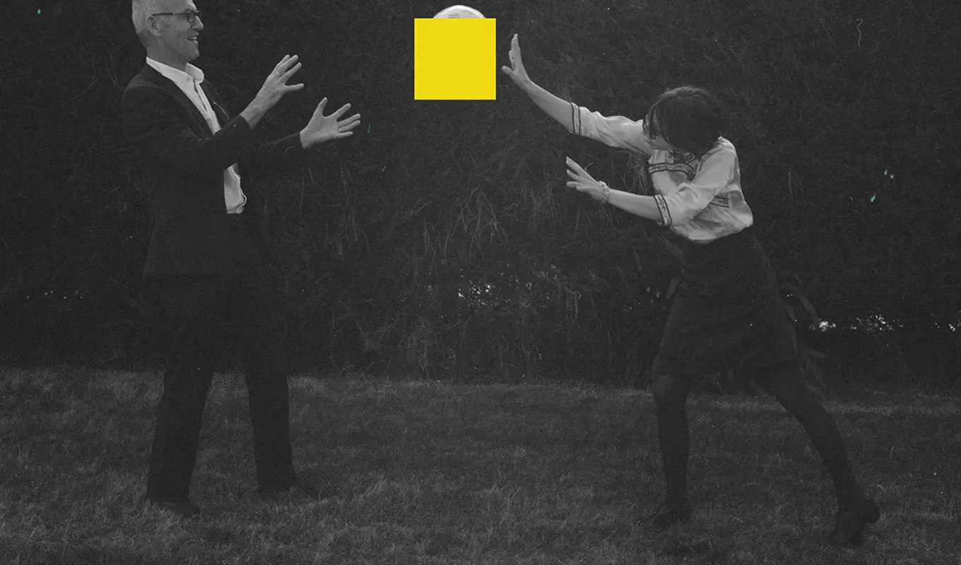 A black and white image of two people throwing an object to each other, the object has been covered with a bright yellow square.