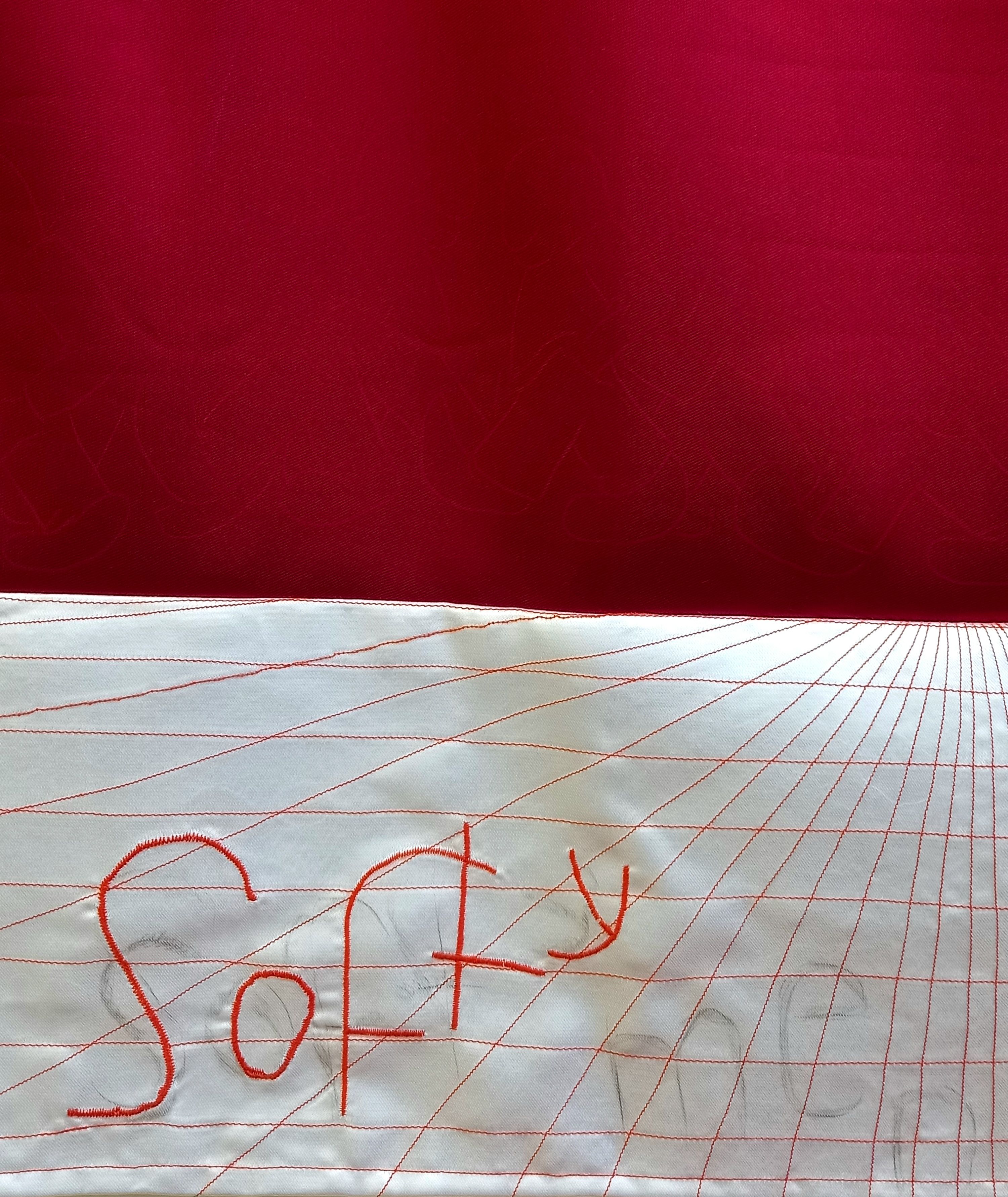 The top half of the image is a deep red and the bottom half features an embroidered grid that distorts into the background. The word 'softy' is embroidered on top of the grid with faint pencil markings of the words 'softy' and 'men'.