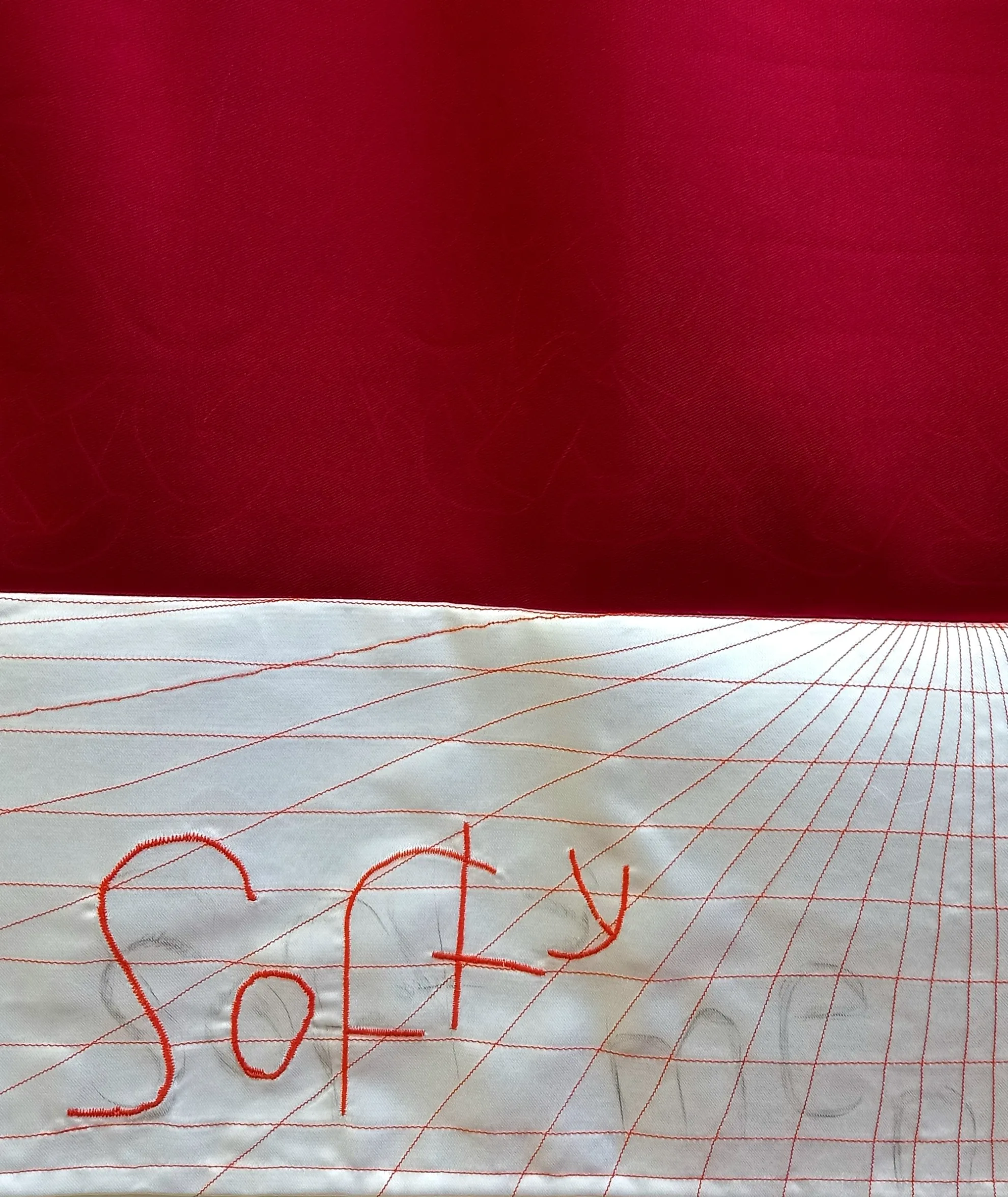 The top half of the image is a deep red and the bottom half features an embroidered grid that distorts into the background. The word 'softy' is embroidered on top of the grid with faint pencil markings of the words 'softy' and 'men'.