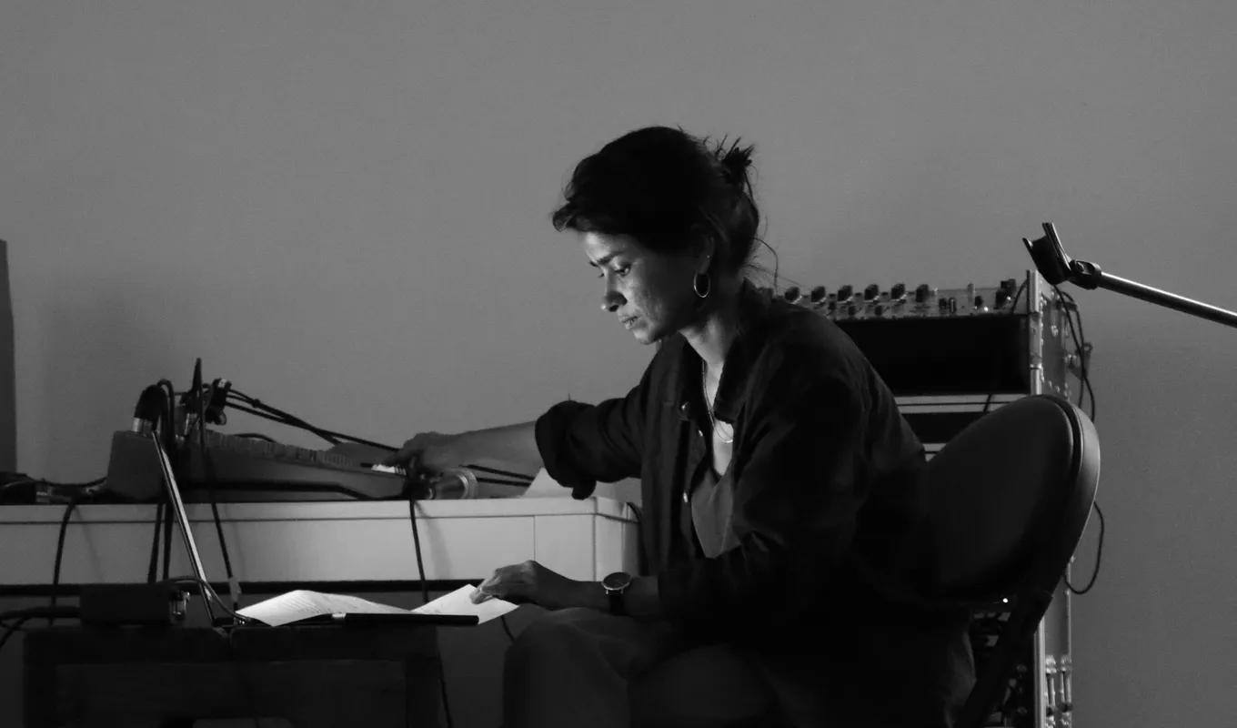 A black and white photo of Aasma Tulika sitting on a chance with sound equipment for her performance.