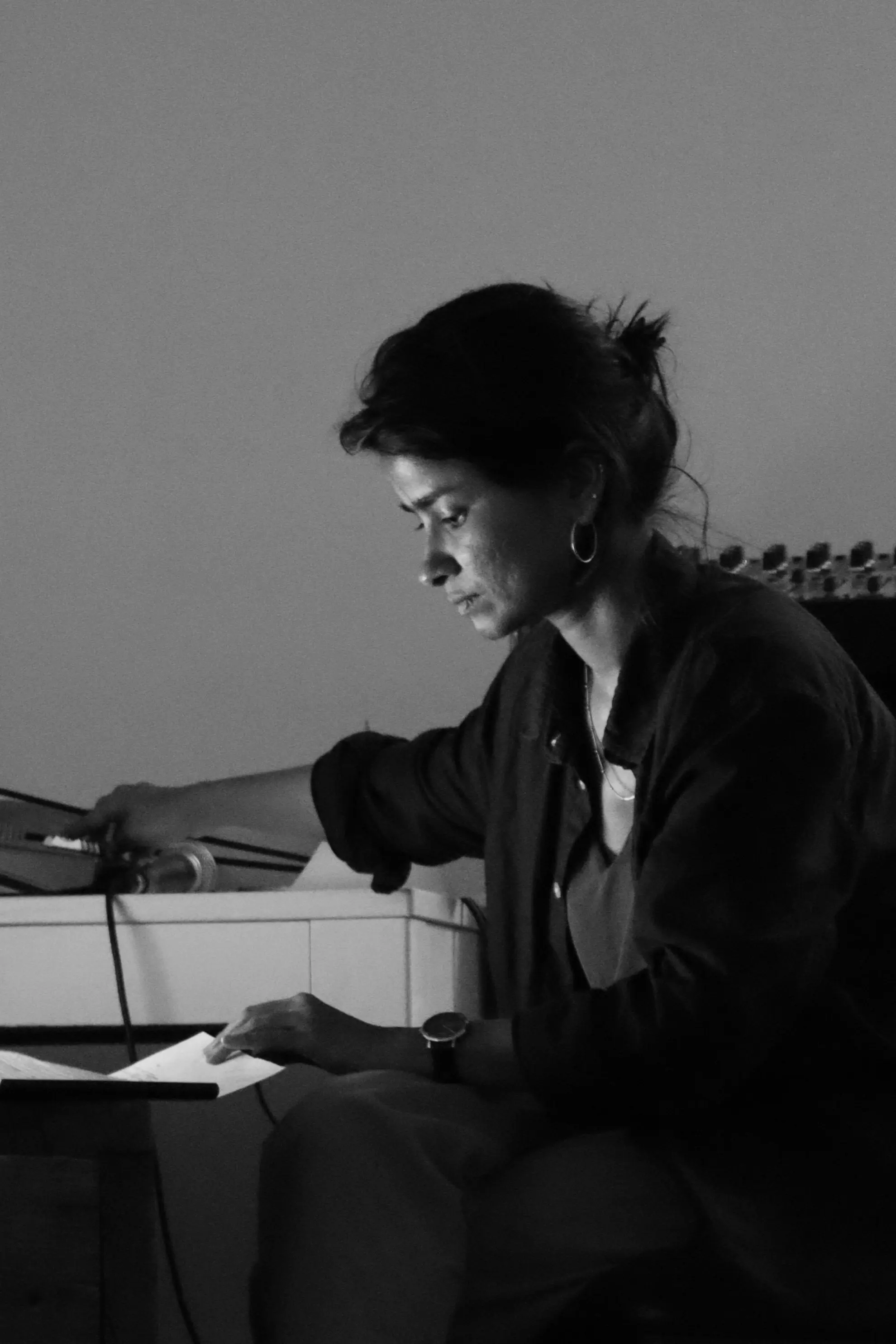A black and white photo of Aasma Tulika sitting on a chance with sound equipment for her performance.