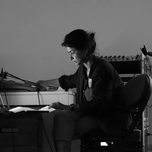 A black and white photo of Aasma Tulika sitting on a chance with sound equipment for her performance.
