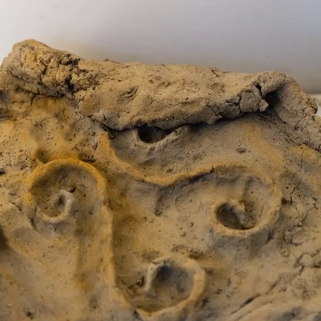 A close up detail of an artwork by Lhotse Collins. The artwork is a slab of unfired wild clay with two swirling lines that has been sculpted into the circular tablet of clay