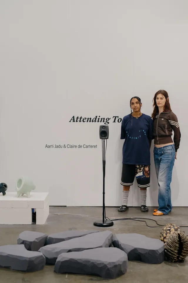 Two artists standing in front of their work - foam sculptures, ceramic piece, and a speaker.
