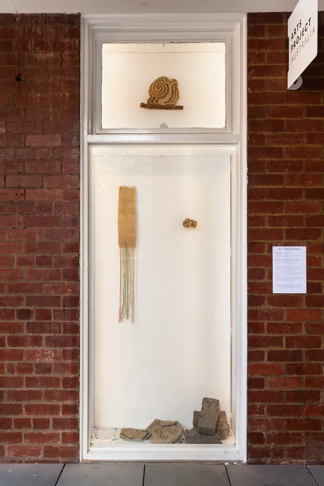 The West Space window installed with several sculptual works and 1 long weaving. The window is surrounded by red bricks