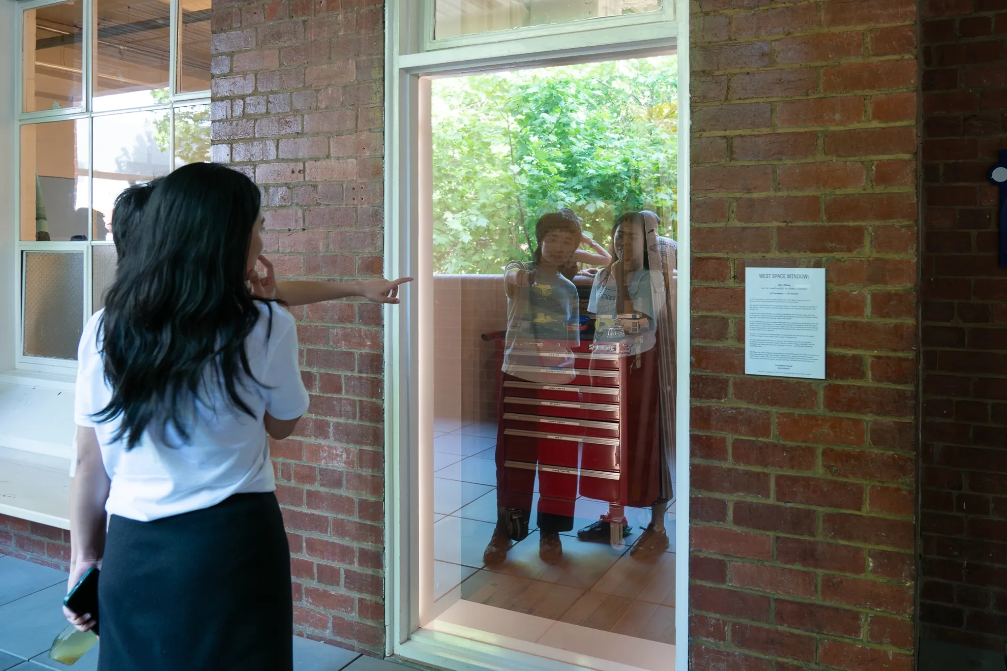 2 figure stand in front of a reflective glass surface. One is pointing and is able to seen in the reflection.