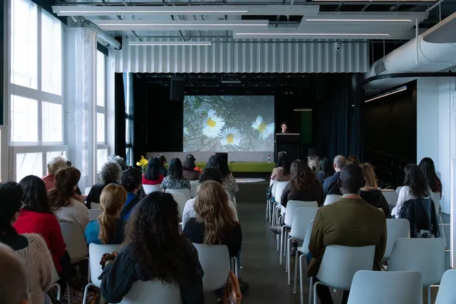 A person presenting performance lecture on the stage through the screen to a group of people.