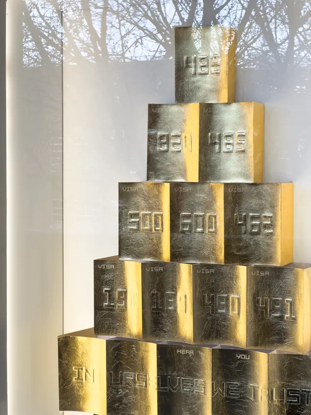 A close up detail of an artwork presented in the west space window. There is a pyramid style stack of gold embossed boxes with a collection of 3 digit numbers representing Australian immigration visa codes.