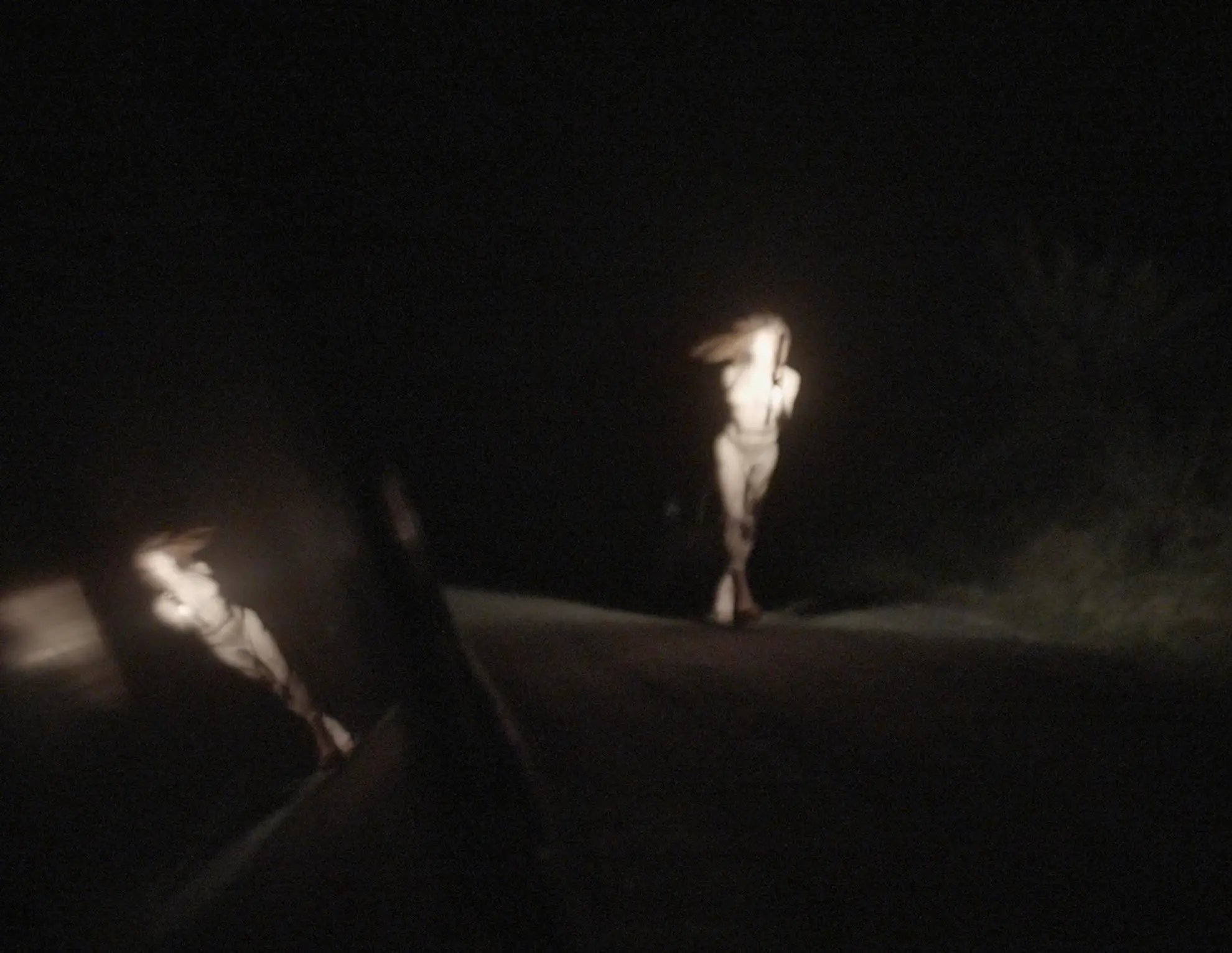 An illuminated Andrea runs alongside a car, on the road in the darkness of night.