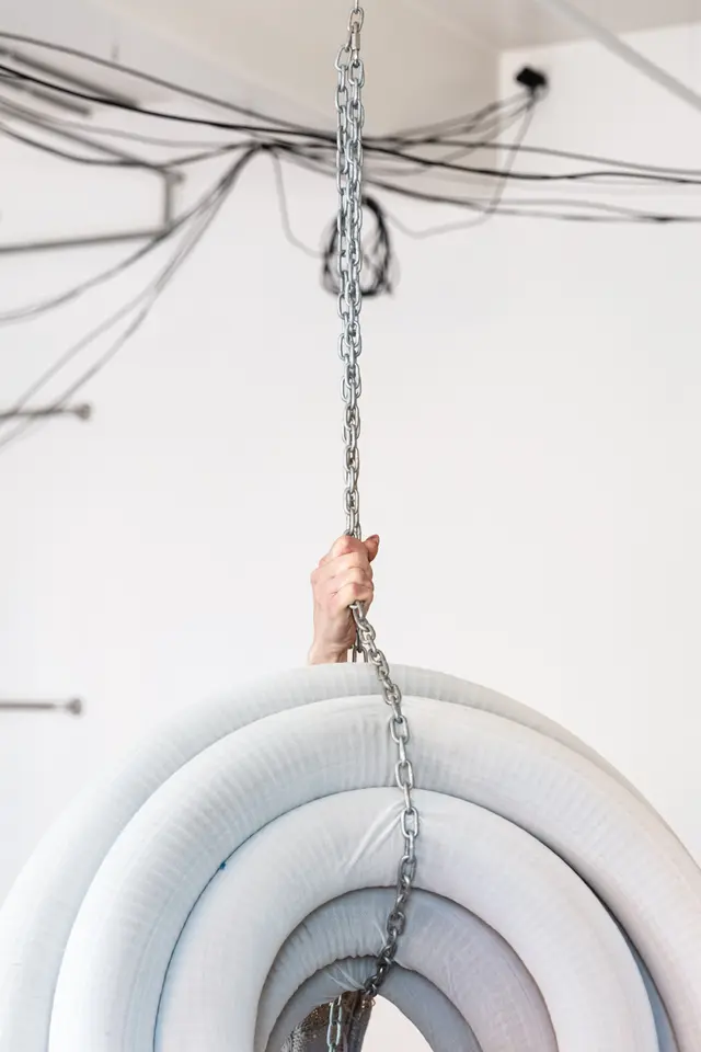 A coil of plastic pipe that is suspended from the ceiling with chains. A hand is holding the chains.