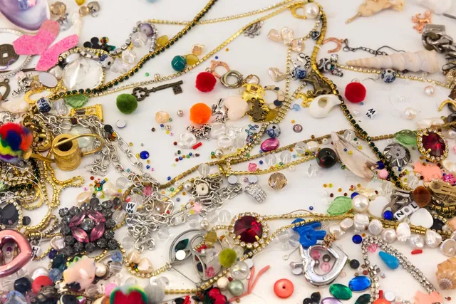 A detail from Matilda Davis' installation "I’ll Leave a Secret in the Window for You: Painting Grotto". The image shows an assortment of trinkets including jewellery, chains, beads, keys, hearts and gems.