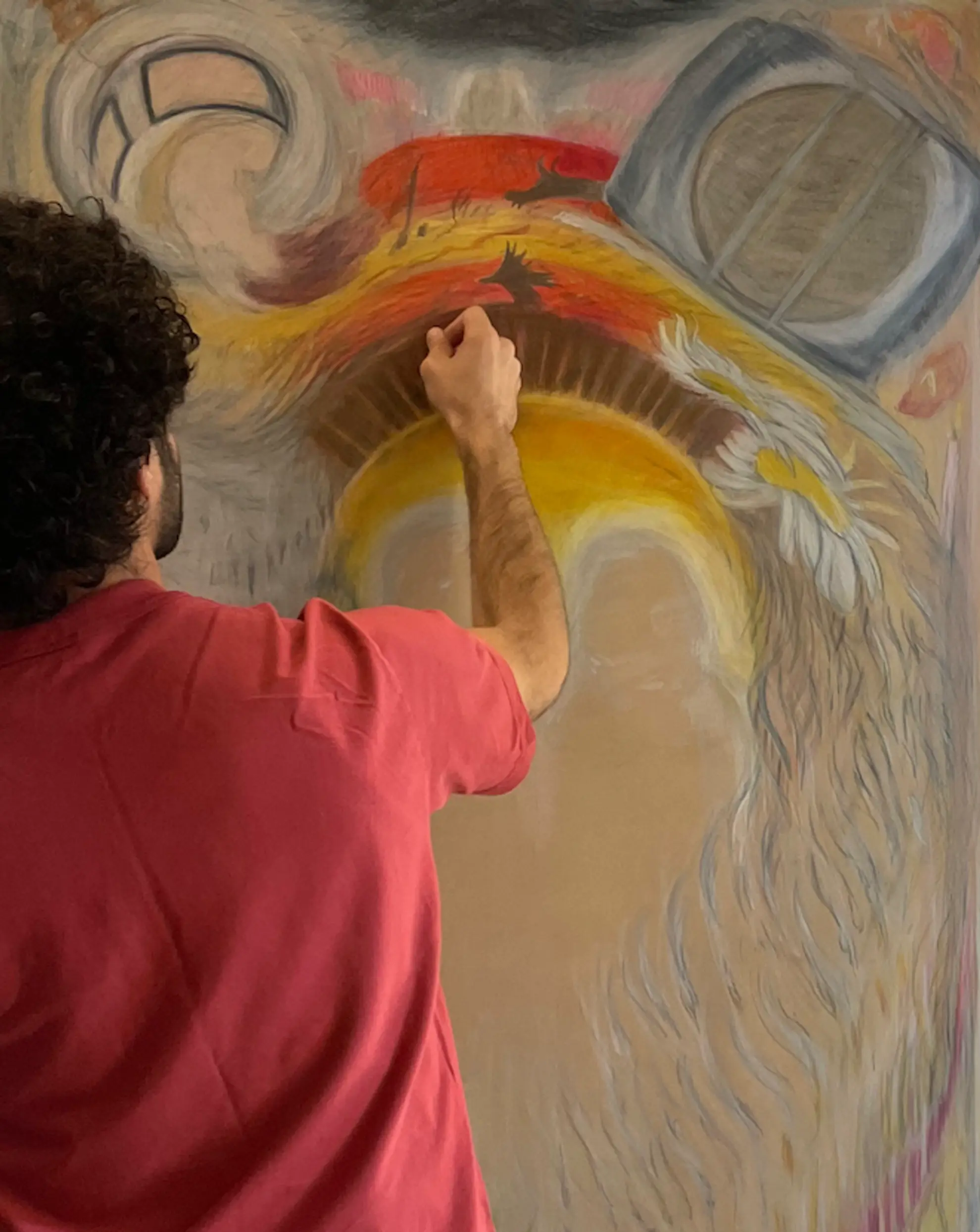 A back view of Khaled Chamma drawing a colourful artwork onto a sheet of paper on a wall.