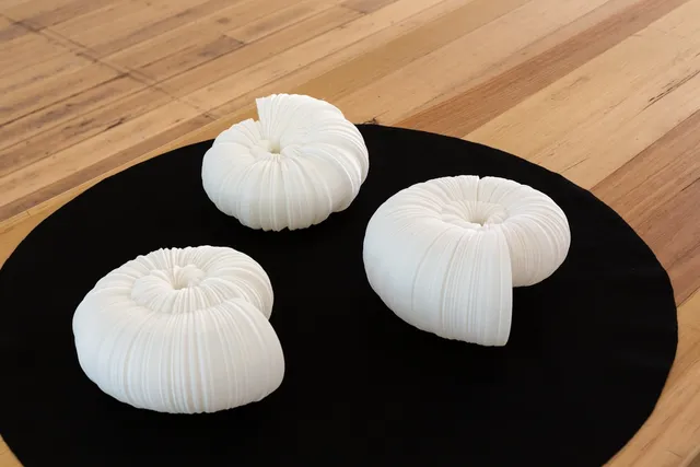 Three shell-shaped white sculptures on a round black base.