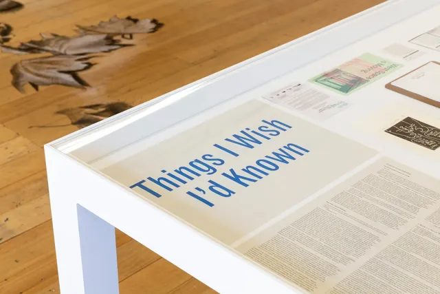 The words 'Things I Wish I'd Known' in thick, blue text printed on paper, placed at the top corned of a glass cabinet table.