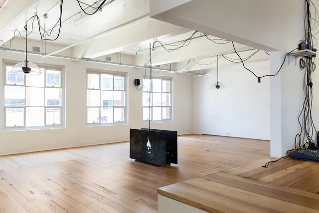 2 large screens stand on the floor of West Space Gallery. There are black cords that drape across the roof and all around the space.