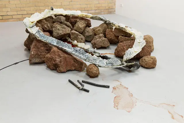 A collection of odd shaped metal castings lay on top of a pile of volcanic rocks