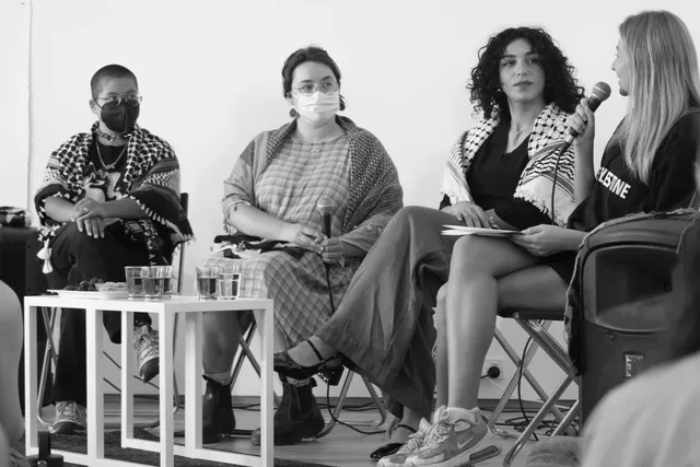 A black-and-white image of four panellists, the person at the right is speaking with a microphone.
