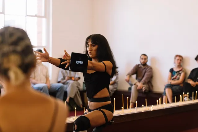 Ari performing in front of a row of lit candles. She has an ipad attached to her wrist that has text on the screen that says "River".