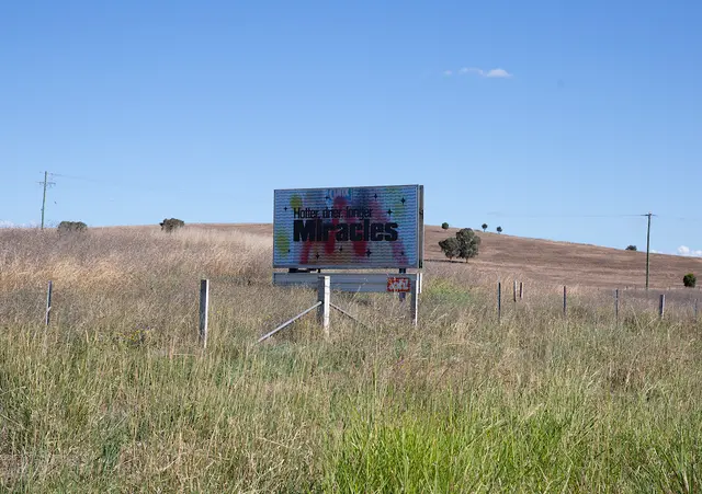 The billboard is positioned in a country setting with blue a sky, long grass