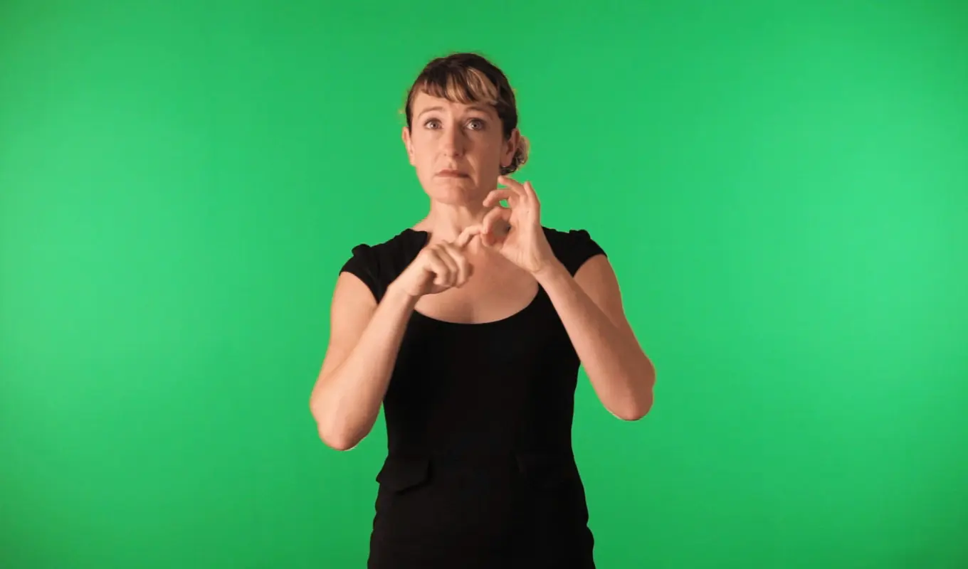 A person signalling with their hands in front of a green screen.