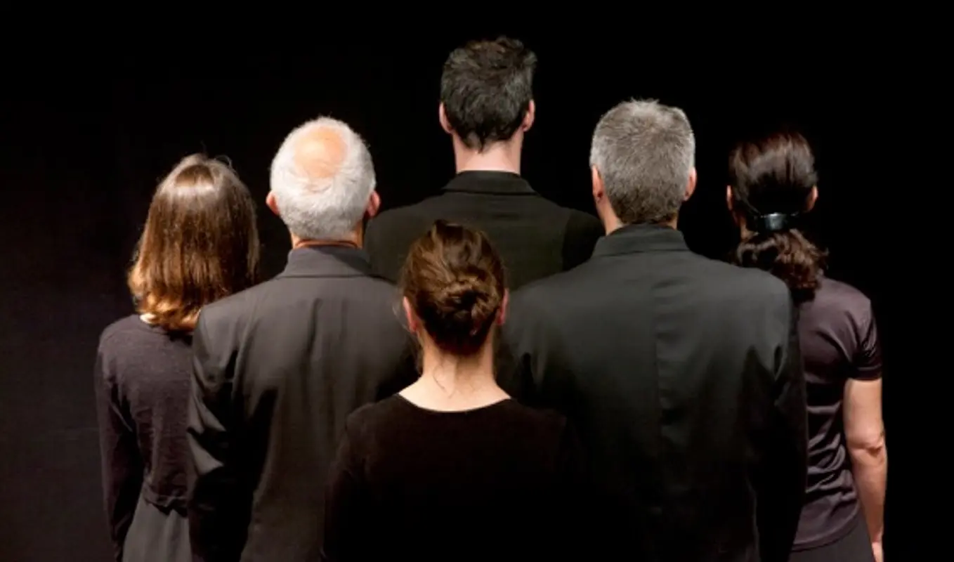 Back view of a group of six people standing close together in a cluster.