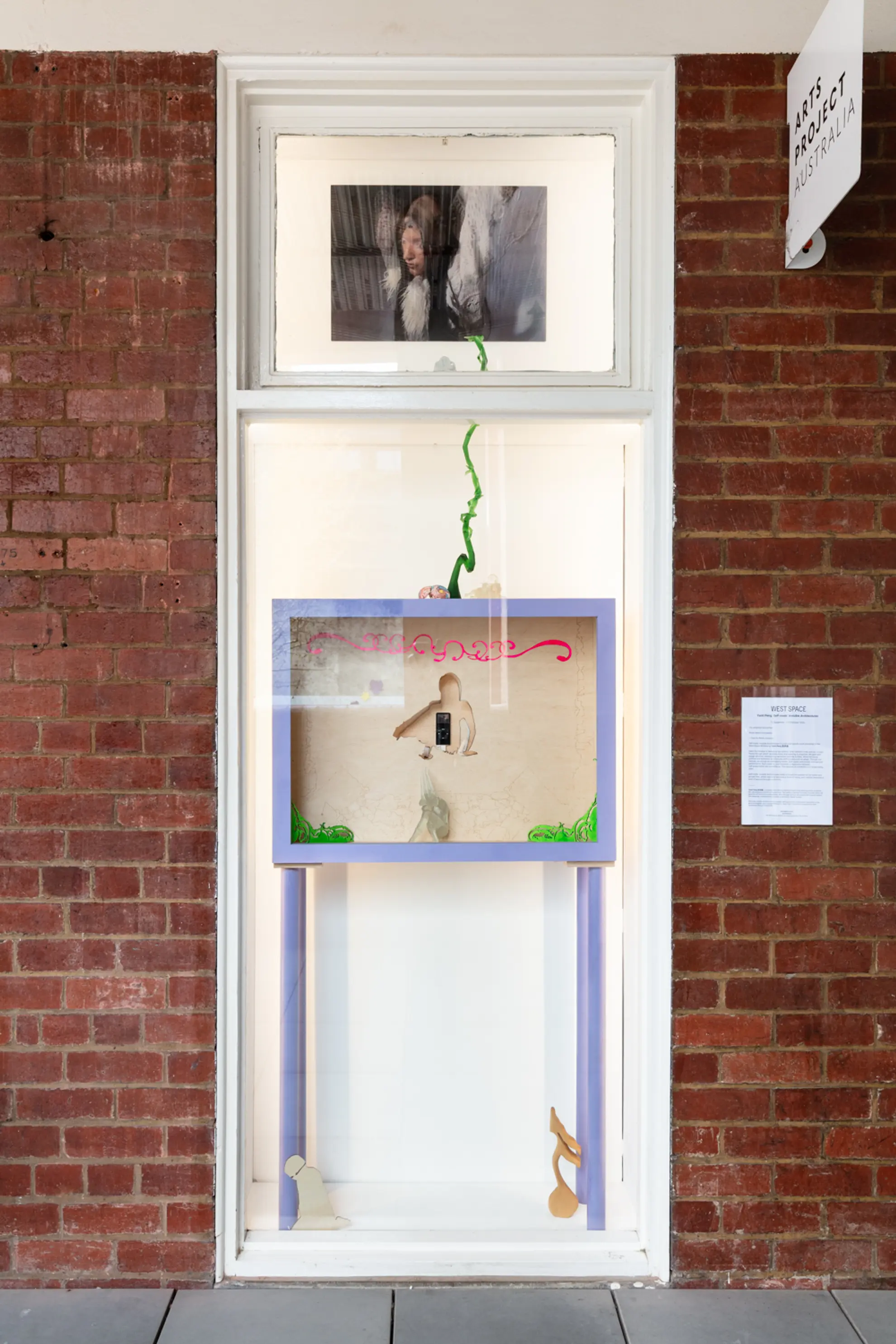 Install view of the West Space window showing a photographic work of a figure in the top window and a mixed media sculptural work in the bottom window.