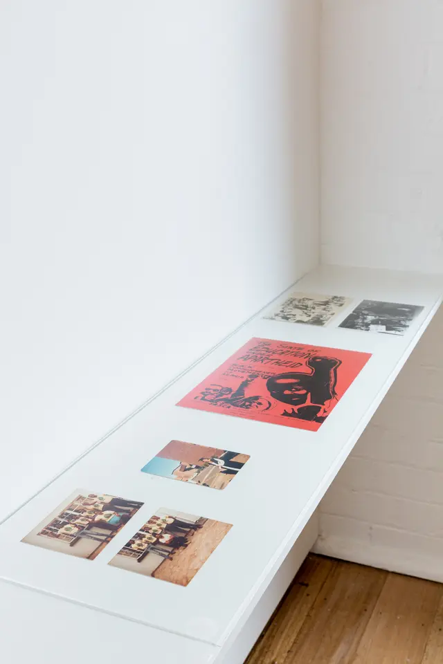 The image shows 3 colour photographs a poster and 2 black and white photos sitting on a shelf in the corner of West Space Gallery.