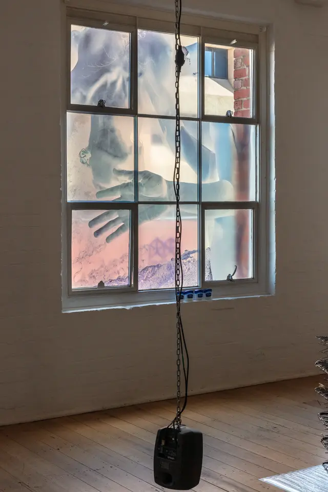 A speaker is suspended from the ceiling. A negative photo of a woman is displayed on the gallery windows.
