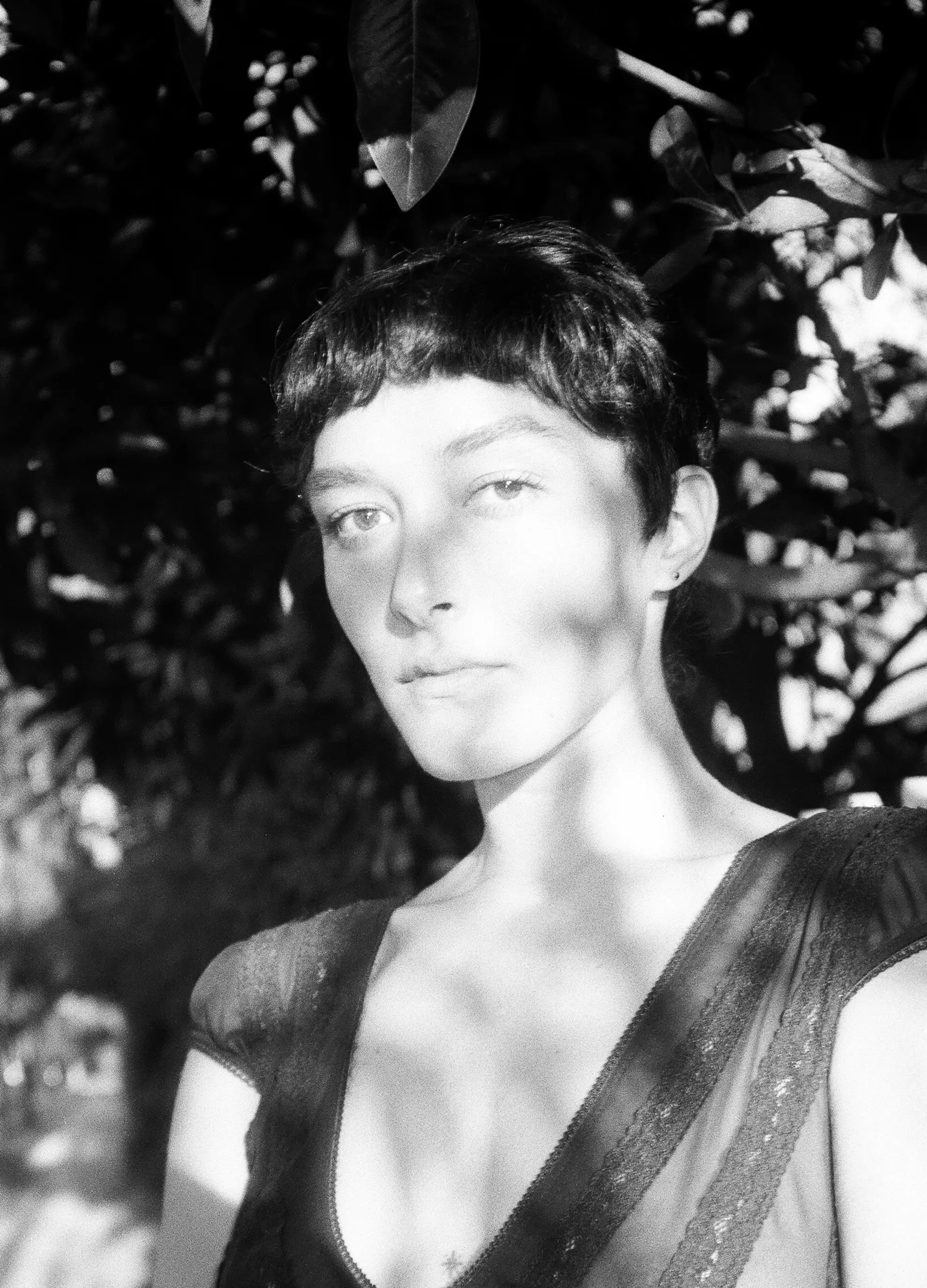 A close-up black and white portrait photograph of Ella Ferris dappled in sunlight and looking at the camera.