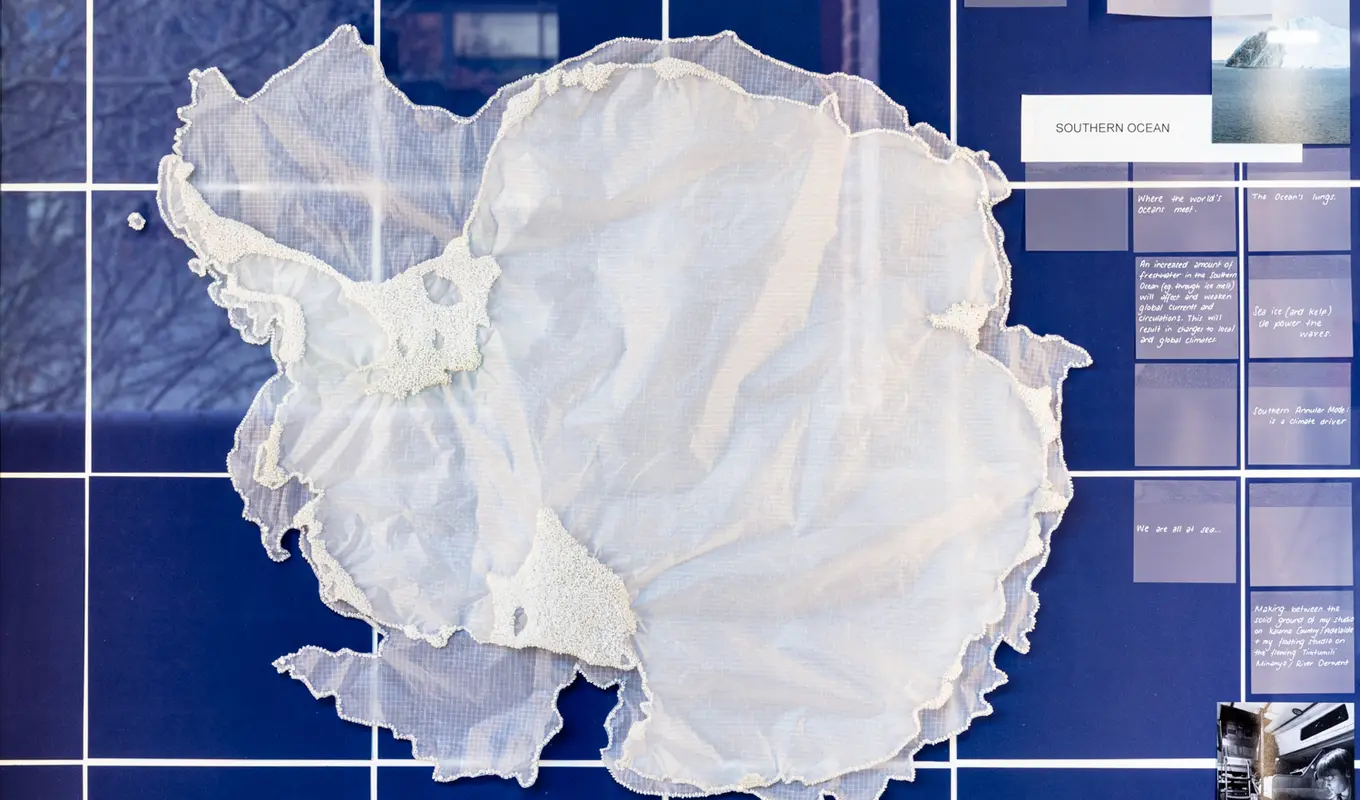 On a background of deep blue squares with white intersections an organic layering of sheer crinkled fabric sits in the middle of the frame. There is some additional texture created by beads around the edges of the material. On the right there are more squares of a muted blue tone with white text and photographs.