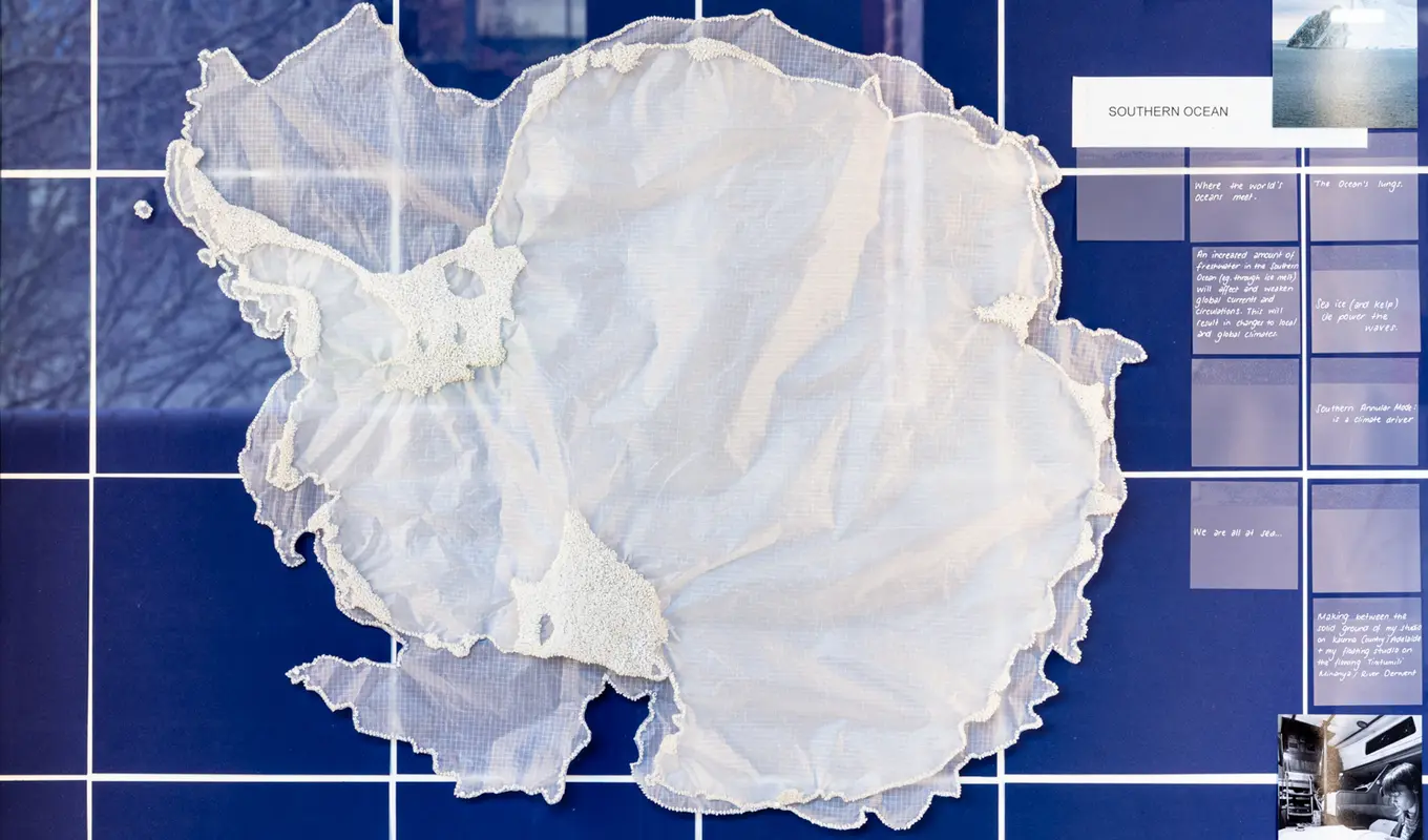 On a background of deep blue squares with white intersections an organic layering of sheer crinkled fabric sits in the middle of the frame. There is some additional texture created by beads around the edges of the material. On the right there are more squares of a muted blue tone with white text and photographs.