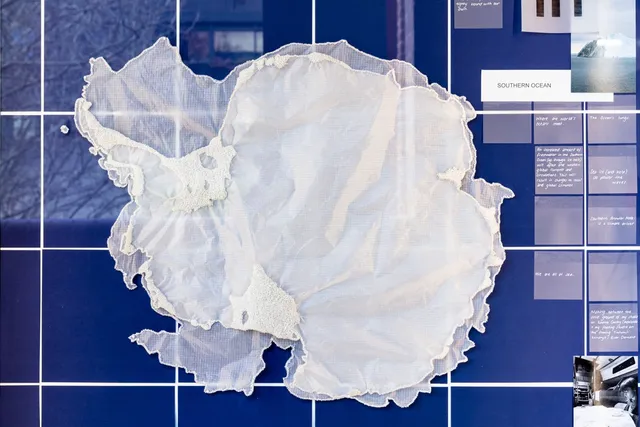 On a background of deep blue squares with white intersections an organic layering of sheer crinkled fabric sits in the middle of the frame. There is some additional texture created by beads around the edges of the material. On the right there are more squares of a muted blue tone with white text and photographs.