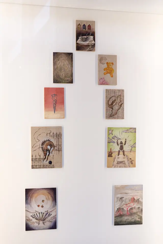 Installation view of Matilda Davis' "I’ll Leave a Secret in the Window for You: Painting Grotto". The installation shows 11 small paintings behind a glass panel.