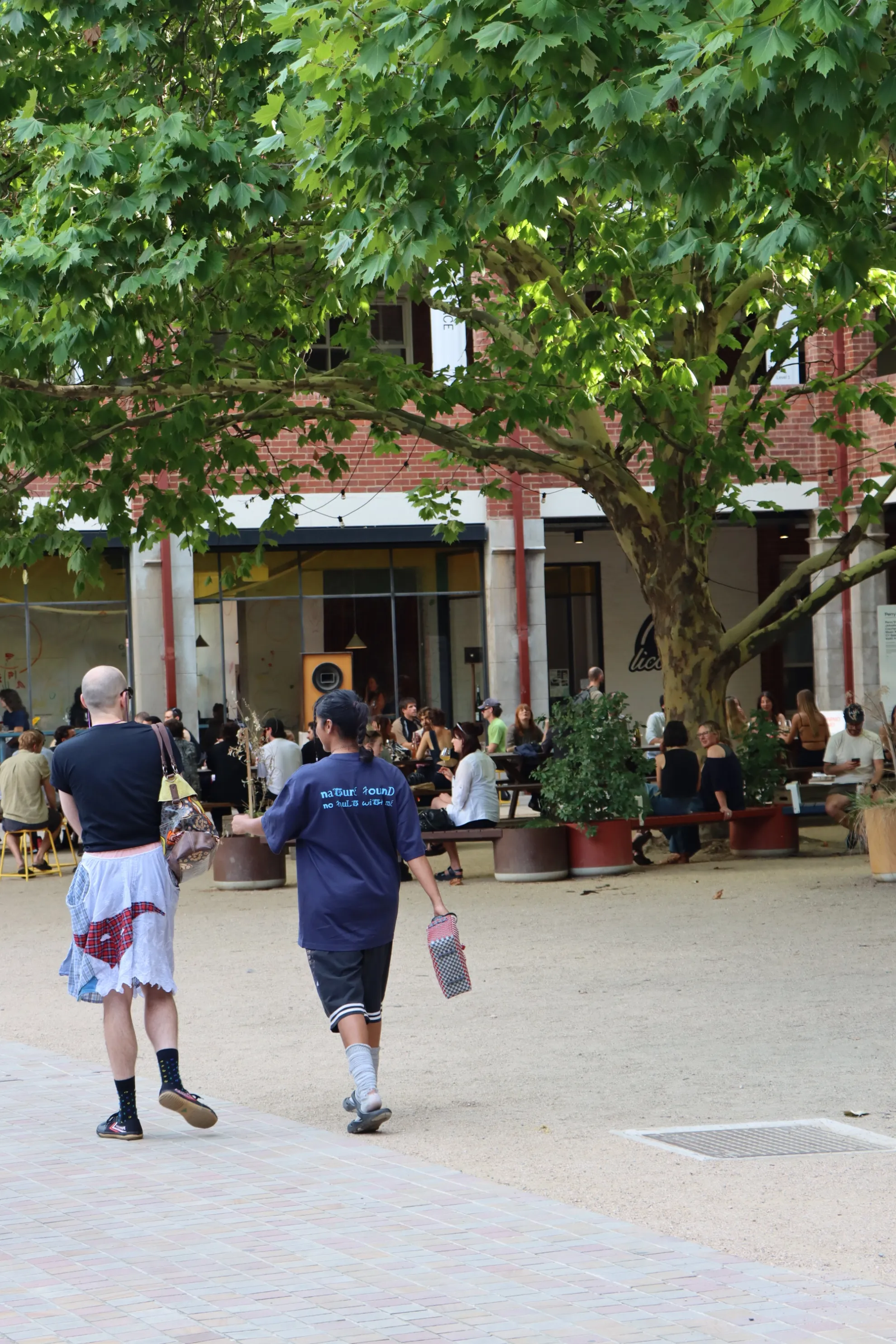 A picture of Collingwood Yards with two people walking along the courtyard and lots of people seated at the long wooden tables.