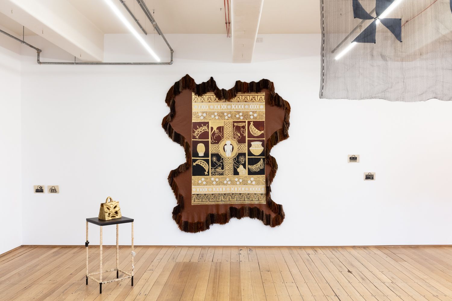 installation view of spilt milk showing  a large wall textile leather work and a collection  of ceramic objects, some on the walls  and some on some plinths.