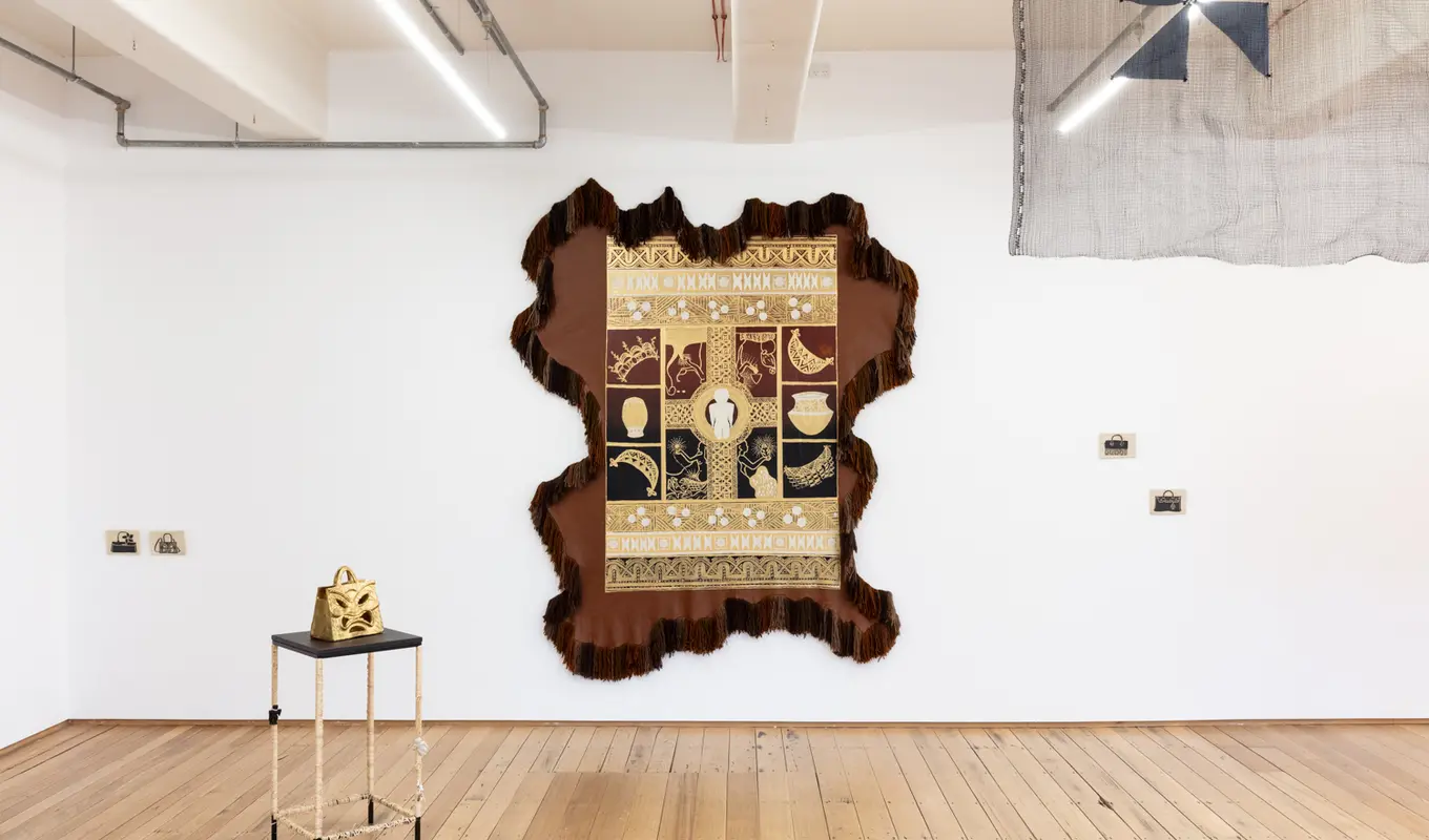 installation view of spilt milk showing a large wall textile leather work and a collection of ceramic objects, some on the walls and some on some plinths.