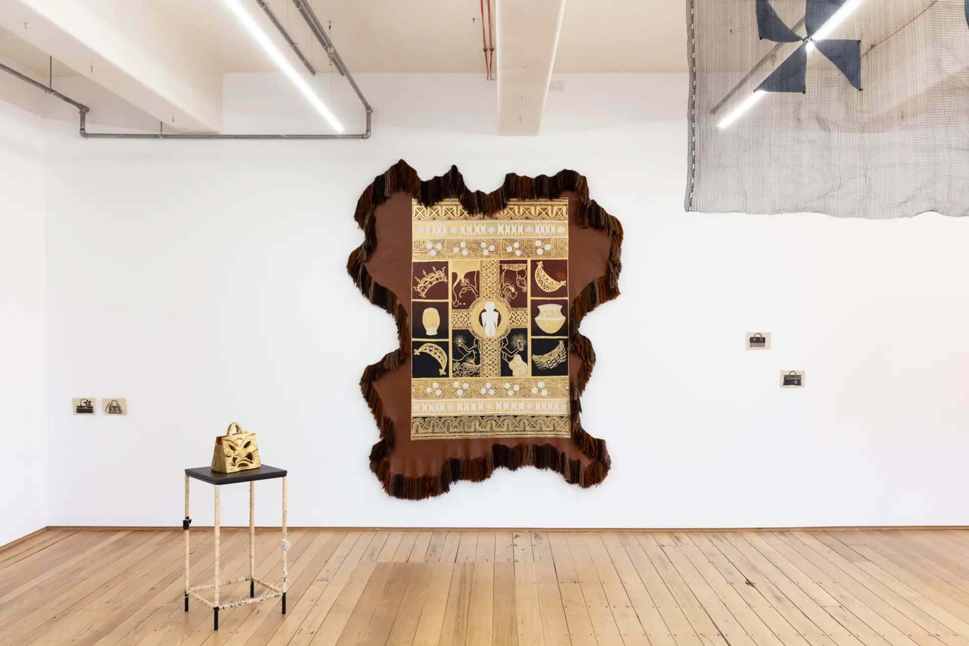 installation view of spilt milk showing a large wall textile leather work and a collection of ceramic objects, some on the walls and some on some plinths.