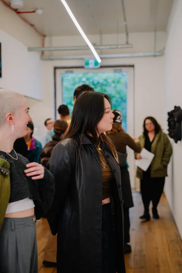 two figures stand in a crowded gallery space looking adoringly at an artwork that is just out of frame. Both figures are smiling