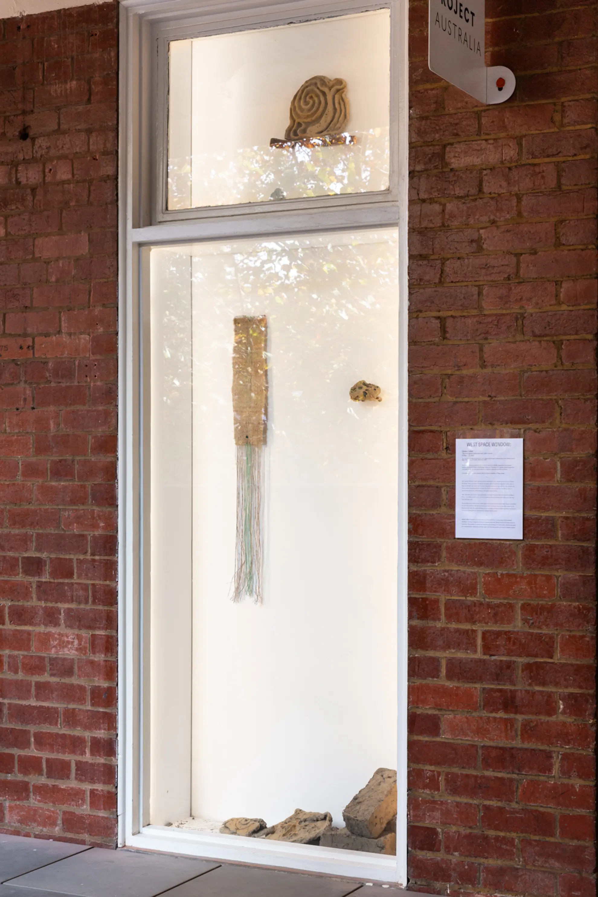 The West Space window installed with several sculptual works and 1 long weaving. The window is surrounded by red bricks