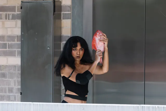 Ari holding a fish like a loaded gun standing in front of silver elevator doors at the Collingwood Yards.