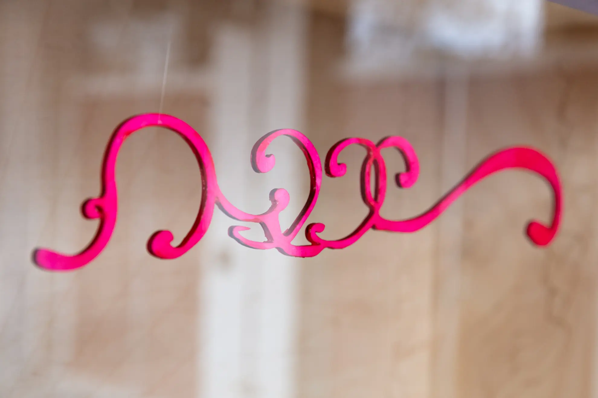 a pink decorative ornate cut out wooden pattern hangs by invisible fishing line as part of the installation in the West Space window