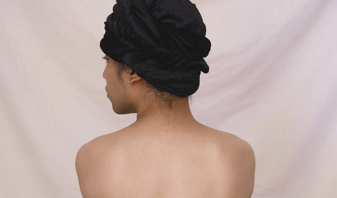 Back view of a partially nude figure wearing a black hair turban and a black and cream skirt.