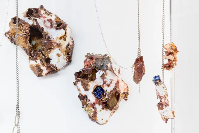 Five marbled porcelain and ceramic sculptures hang from chains against white background.