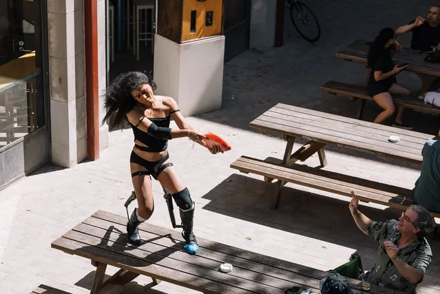 Ari standing on top of a wooden table holding up an orange fish as if it were a gun. In front of her and audience member has their hands up as if to say 'dont' shoot'.