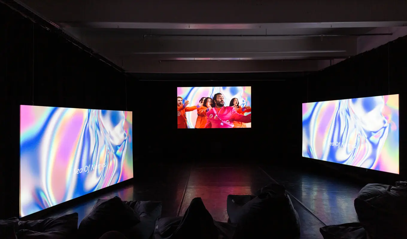 Artist HOSSEI's audio-visual artwork THUNDERBLOOM. Three screens glow with the projected images of performers, bright backgorund colours and captioned lyrics.