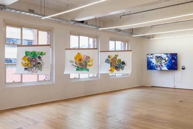 Three paintings hung in line from the ceiling near the windows, video played on a TV in the back.