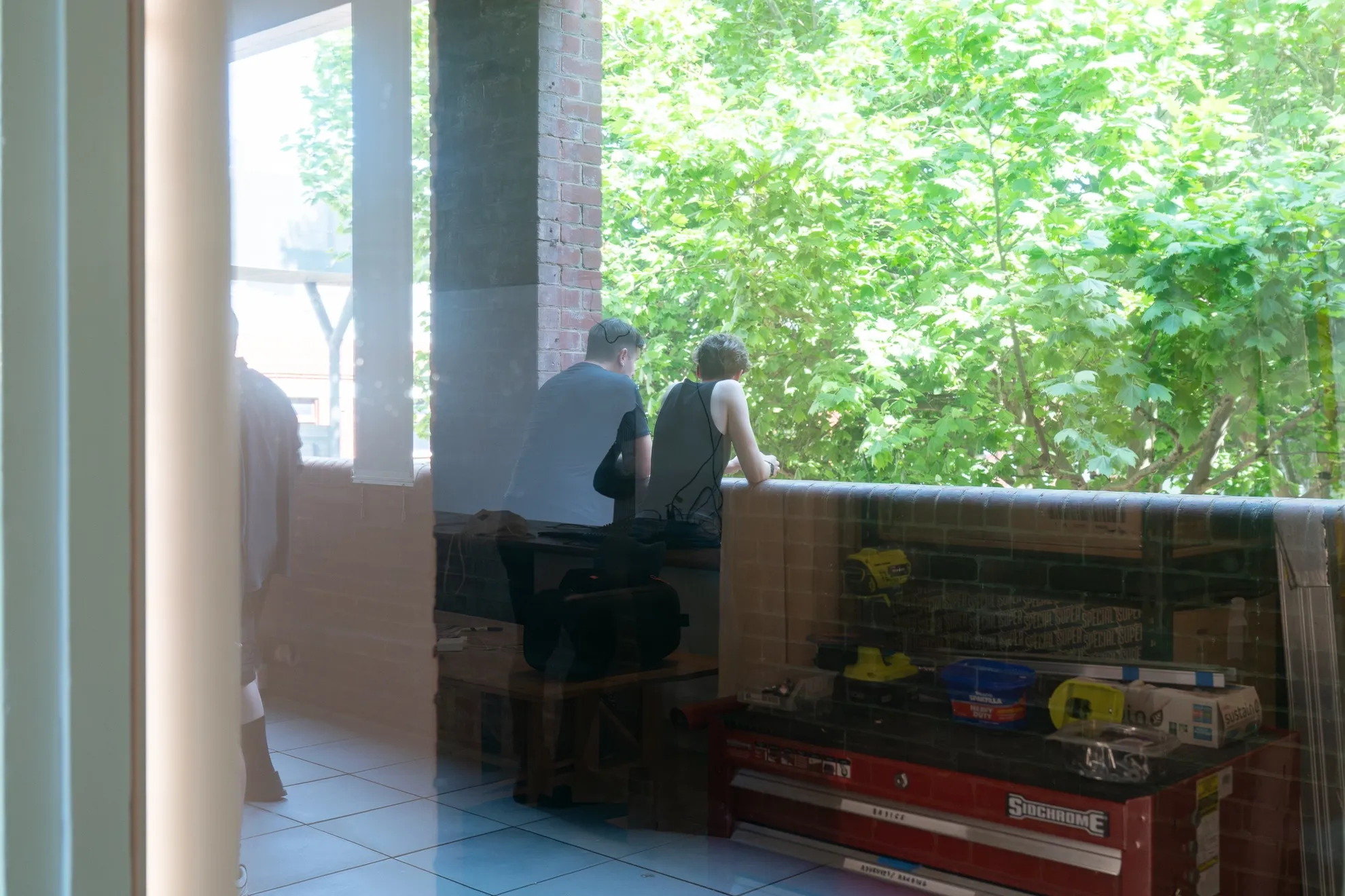 The back of two people leaning toward the balcony wall viewed through the glass window.